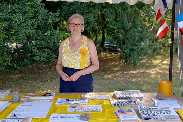 Jenny Wilkinson at a table of campaign materials with shrubs in the background